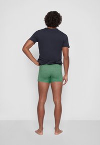 Grüne Baumwollboxershorts mit meliertem Muster und enger Passform, kombiniert mit einem marineblauen T-Shirt mit kurzen Ärmeln, von hinten betrachtet.