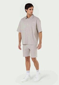 Camisa de manga curta riscada e calções correspondentes em bege claro, feitos de tecido leve. Apresenta uma frente com botões e um corte descontraído.