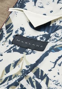 Weißer Stoff mit navy- und beige-farbigen abstrakten Blattmustern, versehen mit einem schwarzen Etikett mit dem Wort "MARLANE" in weißem Text.