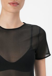 Top nero trasparente con maniche corte, scollatura rotonda e silhouette aderente. Presenta una sovrapposizione in tessuto a rete testurizzata.