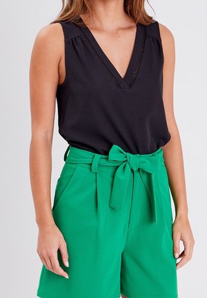 Femme portant un haut noir sans manches à encolure en V et un short vert taille haute avec une ceinture en tissu nouée à la taille.