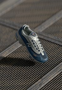 Blue and gray New Balance 1000 sneaker with a mesh upper, textured sole, reflective accents, and prominent lacing system.