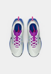 Αθλητικά παπούτσια Nike με ανοιχτό γκρι επάνω μέρος από δίχτυ, μοβ κορδόνια και λεπτομέρειες, μπλε σόλα και αντίθετο μπλε εσωτερικό με λογότυπο.