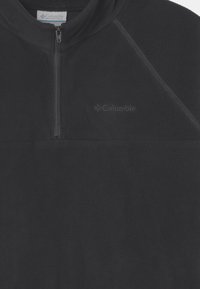 Pullover in pile nero con zip a quarti nella parte anteriore, tessuto testurizzato e dettagli cuciti. Presenta un logo nell'angolo in alto a sinistra.