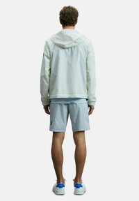 Veste légère à capuche blanche, assortie à un short bleu clair. La veste possède des poignets élastiques et un ourlet à cordon de serrage ; le short présente un logo sur le côté.
