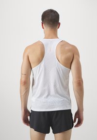 Canotta atletica bianca con texture in rete traspirante e design a schiena scoperta, completata da dettagli con motivi sottili.