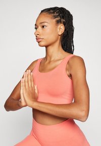 Koral atletisk crop top og høyere midje leggings laget av glatt, elastisk stoff; tettsittende design med brede stropper og sømløs konstruksjon.