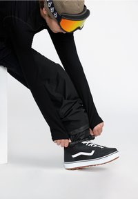 Des baskets montantes noires avec des accents blancs et des semelles en caoutchouc. La personne porte un pantalon ajusté et un haut à manches longues.