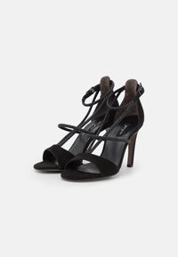 Sandalias de tacón alto de ante negro con un diseño con tiras y hebilla en el tobillo. Cuentan con una punta abierta y correas texturizadas para un detalle adicional.