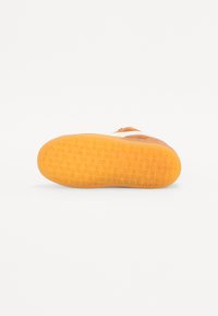 Sål i oransje gummi med teksturert mønster, som har mønstrede grep for bedre feste. Glatt øvre område med minimale designelementer.