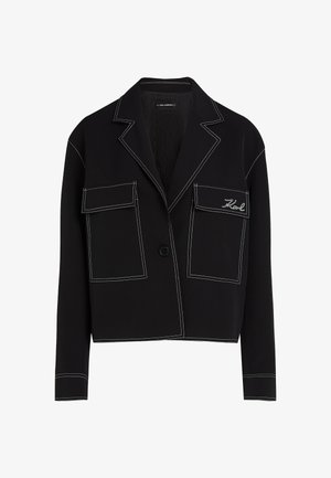 Veste noire courte en tissu lisse, avec des coutures blanches, deux poches avant et une fermeture à boutons. Détail de logo brodé inclus.