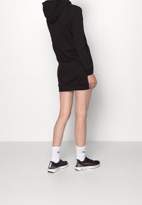 Vestido sudadera negro con capucha, bolsillo canguro, puños y bajo acanalados. Combina con zapatillas negras y calcetines blancos. Diseño minimalista, sin gráficos.