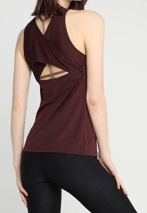 Kobieta nosząca bordowy top bez rękawów z wycięciem w kształcie klucza i paskiem z tyłu, w połączeniu z czarnymi legginsami.