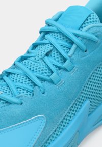 Blå atletiksko med net- og ruskindsmaterialer, flade snørebånd, polstret tung og glatte gummiaccenter. Teksturerede designelementer.