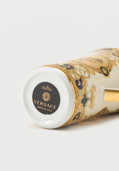 Πορσελάνινο κύπελλο Versace Prestige Gala με περίτεχνο χρυσό και μαύρο μπαρόκ σχέδιο, ξαπλωμένο στο πλάι και δείχνει την ετικέτα με την επωνυμία από κάτω.