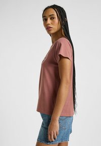 Camiseta de algodón rosa con mangas cortas, con cuello redondo y un estampado gráfico en la parte delantera, combinada con pantalones cortos de mezclilla.