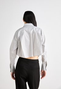 Camicetta cropped con righe verticali bianche e nere, maniche lunghe e dettagli ricamati sul retro, abbinata a pantaloni neri.