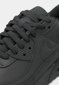 Schwarzer Nike-Sneaker mit einem strukturierten Lederobermaterial, runden Schnürsenkeln und Belüftungslöchern. Das Design umfasst dezente Markenakzente.