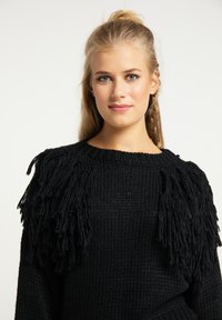 Pulover negru tricotat, cu țesătură texturată, cu accente lungi de franjuri la umeri și un gât rotund.