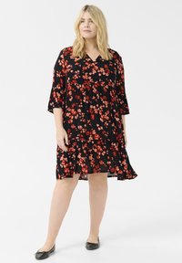 Vestido negro con flores rojas y rosas, con dobladillo en capas y escote en V. Presenta mangas tres cuartos y una tela ligera y fluida.