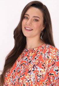 Färgglad blommönstrad topp i livlig orange, med rund halsringning och korta ärmar, i en mjuk tygtextur och avslappnad passform.