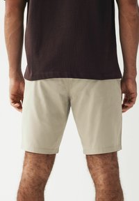 Pantalones cortos beige de tejido ligero, con corte recto, bolsillos laterales y un dobladillo que termina por encima de la rodilla.