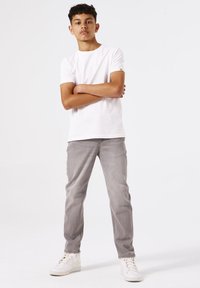 Camiseta blanca de manga corta combinada con vaqueros gris claro y zapatillas blancas. Diseño simple sin patrones. La tela parece suave y casual.