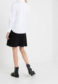 Camicia bianca con maniche a sbuffo, abbinata a una gonna nera svasata e stivaletti neri sopra la caviglia con fibbie e dettagli testurizzati.