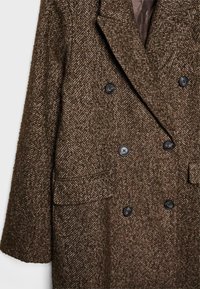Manteau marron en chevrons à double boutonnage, fabriqué en tissu texturé, avec des boutons noirs, des revers crantés et deux poches avant.