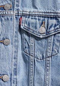 Ljusblå denimjacka med silverknappar, bröstficka och synlig söm. Sliten yta med en klassisk design.