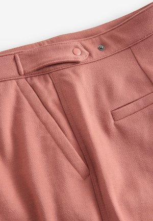 Roze op maat gemaakte broek met een textuurstof, plooien aan de voorkant, een klein voorzakje en een knoopsluiting bij de taille.