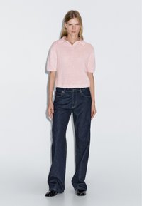Světlounce růžové pletené polo tričko s krátkými rukávy, doplněné širokými tmavě modrými džíny. Tkanina vypadá měkce a má strukturovaný povrch.