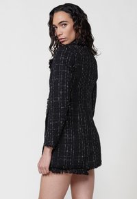 Rochie din tweed negru cu model în carouri albe, cu mâneci lungi și tiv desfăcut. Material texturat; design mulat; lungime până la mijlocul coapsei.