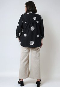 Black shirt with white floral prints, loose fit, long sleeves. Paired with beige wide-leg pants and black heeled sandals.