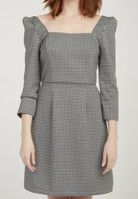 Czarno-biała sukienka w kratkę z kwadratowym dekoltem, bufiastymi rękawami do łokcia i dopasowaną talią, wykonana z teksturowanej tkaniny.