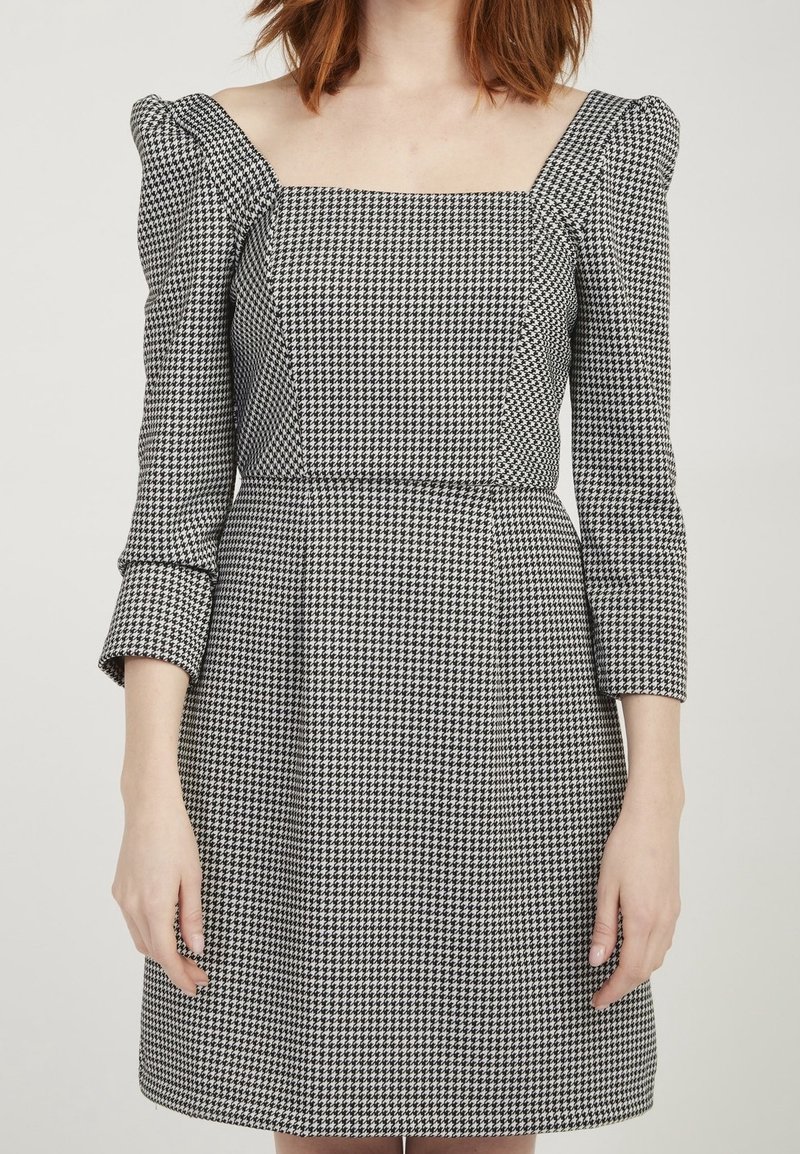 Czarno-biała sukienka w kratkę z kwadratowym dekoltem, bufiastymi rękawami do łokcia i dopasowaną talią, wykonana z teksturowanej tkaniny.