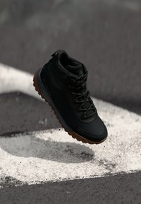 Czarne buty trekkingowe z teksturowaną cholewką, gumową podeszwą i metalowymi oczkami; wyposażone w wyściełany kołnierz i wyróżniające się niebieskie akcenty.