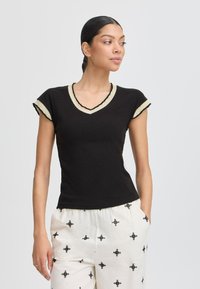 Tricou negru cu decolteu în V, cu mâneci scurte ondulate, având un tiv bej la gât și marginea mânecilor. Design moale, ajustat.