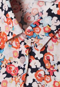 Närbild av en skjortkrage och knappar med ett flerfärgat blommönster i rött, vitt, blått och svart på tyget.