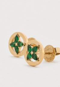 Χρυσά σκουλαρίκια με κυκλικό σχέδιο που διαθέτουν τέσσερις πράσινες πέτρες τοποθετημένες σε σχέδιο λουλουδιού, στερεωμένα με καρφίτσα.