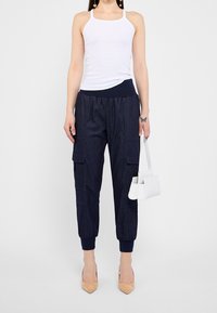 Pantalones cargo azul marino con cintura elástica y tobillos ajustados; combinados con una camiseta sin mangas blanca y un pequeño bolso blanco.
