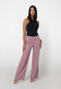 Čierny top bez rukávov s vysokým golierom v kombinácii s svetloružovými širokými nohavicami s textúrovým povrchom a prednými vreckami.