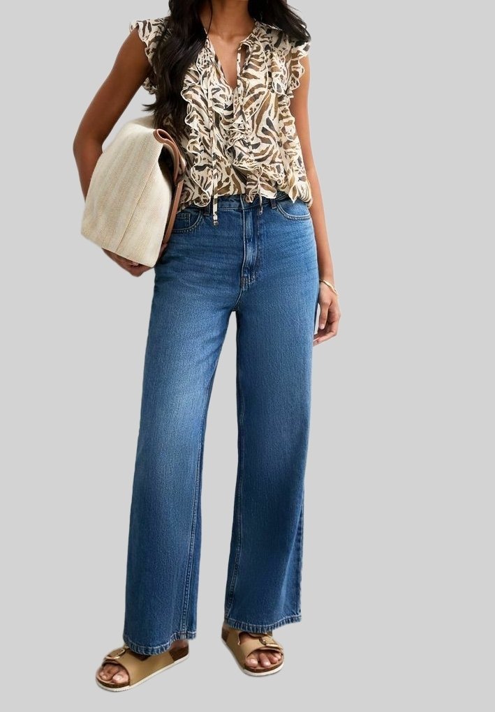 Blommig, rufsig blus i beige och brunt, med blå högmidjade vida jeans. Tan sandaler och en ljus, strukturerad väska.