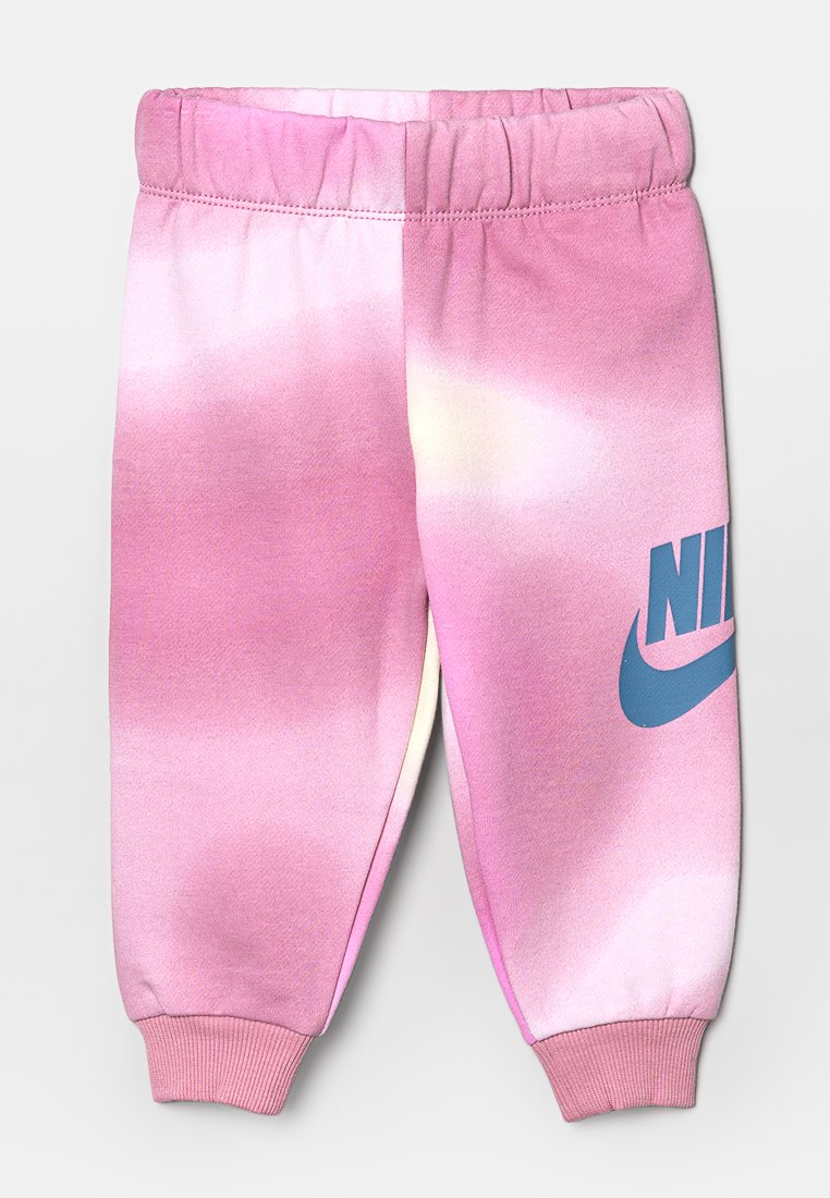Pantalon de survêtement rose tie-dye avec des chevilles resserrées, présentant un logo Nike bleu bien visible sur la jambe gauche sur un fond doux et mélangé.
