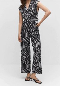 Mono de patrón en blanco y negro con escote en V, mangas cortas, piernas anchas y cintura ceñida con cinturón, fabricado en tela ligera.