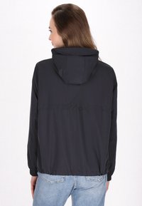 Giacca nera leggera con cappuccio, polsini elasticizzati e orlo regolabile; texture liscia e nessun sistema di chiusura visibile sul retro.