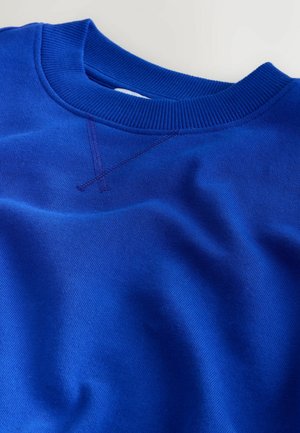 Modrá mikina s kulatým výstřihem, žebrovaným límcem a ozdobným prošitím na hrudi, položená na bílé ploše.