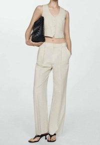 Gilet court rayé beige et pantalon à jambes larges. Le tissu est lisse avec une légère texture, accompagné d'une pochette noire tissée et de sandales à brides.