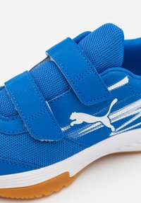 Chaussure de sport bleue avec deux bandes Velcro, tige en maille, logo PUMA et rayures blanches, semelle en caoutchouc avec accents orange.