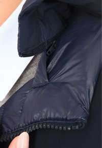 Colletto di giacca puffer navy con texture trapuntata e dettaglio della zip nera, foderato con tessuto liscio. Vista ravvicinata del design del colletto.